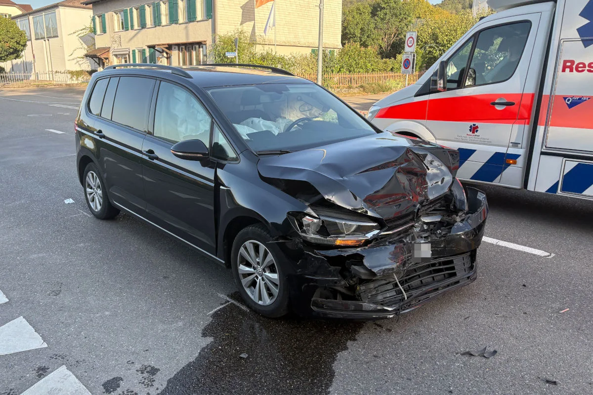 Ein beschädigter schwarzer VW mit stark deformierter Front steht neben einem Rettungswagen, vermutlich nach einem Unfall auf einer Stadtstraße.