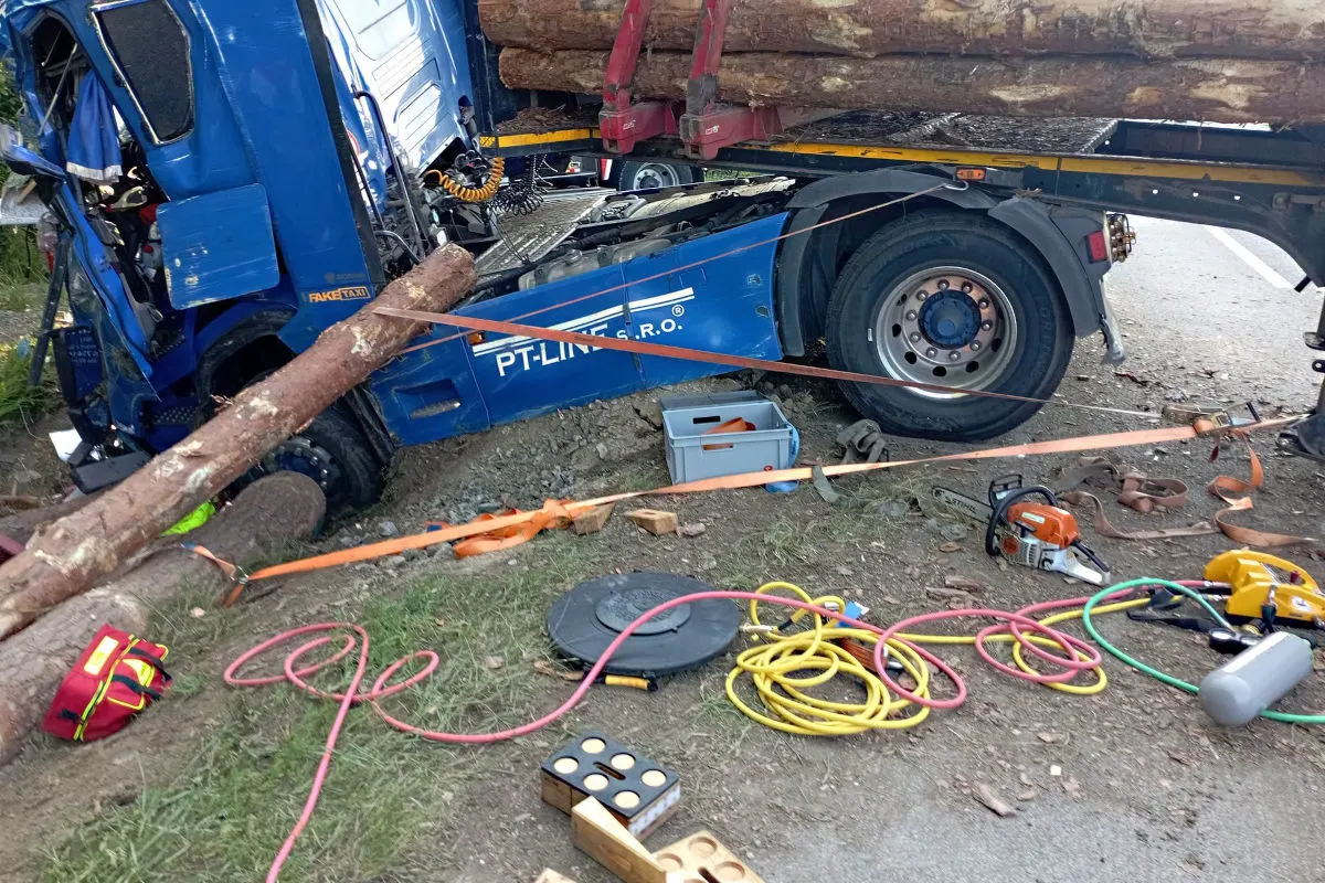 Ein blauer Lastwagen liegt im Graben, beladen mit Baumstämmen. Verschiedene Werkzeuge sind am Boden verstreut.