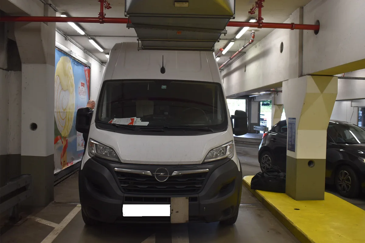 Ein weißer Lieferwagen steckt unter einem Garagentor in einer Tiefgarage fest. Rechts steht ein weiteres Fahrzeug geparkt.