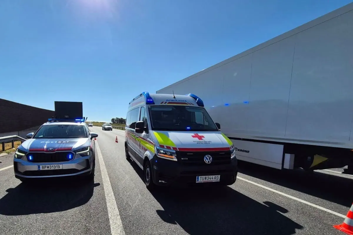 Ein Polizeiwagen und ein Rettungswagen stehen auf einer Autobahn. Die Szene spielt bei klarem Wetter und Sonnenschein.