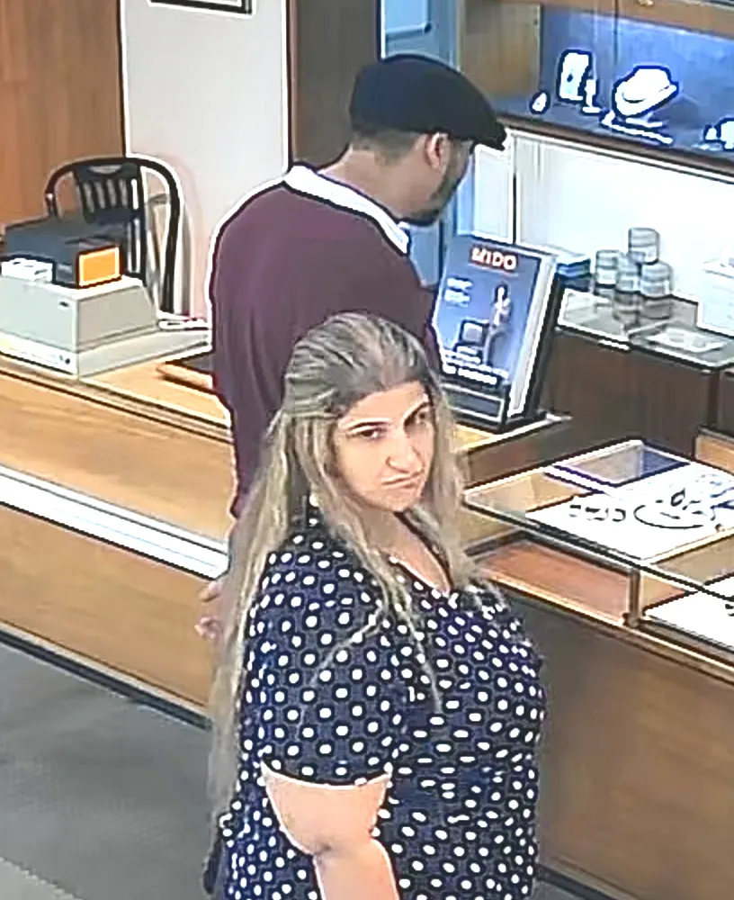 Eine Frau in einem gepunkteten Kleid steht in einem Geschäft mit Vitrinen, während ein Mann im Hintergrund steht.
