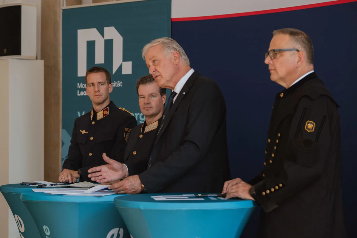 Drei Männer in Uniform und ein weiterer Mann stehen hinter einem Tisch und sprechen, vermutlich während einer Pressekonferenz.