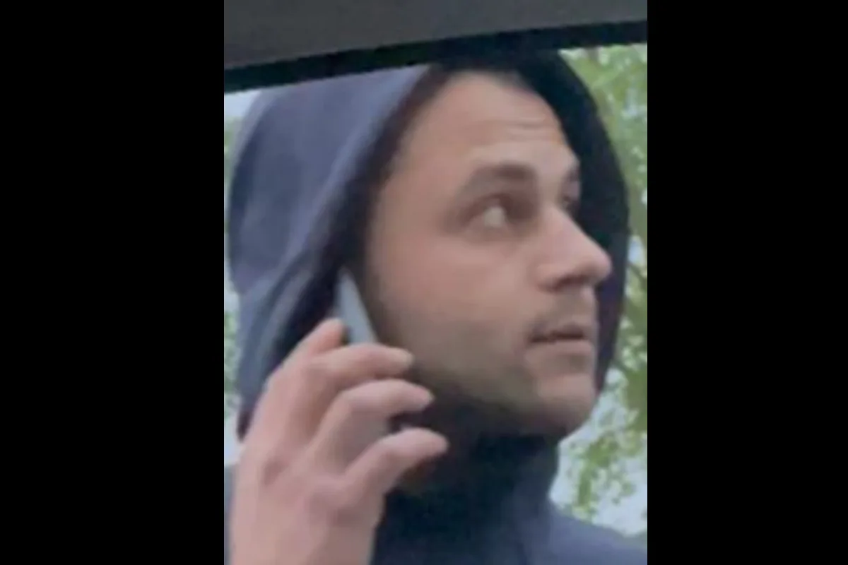Ein Mann in einer dunklen Kapuze hält ein Telefon ans Ohr und schaut zur Seite. Der Hintergrund zeigt einen Baum.