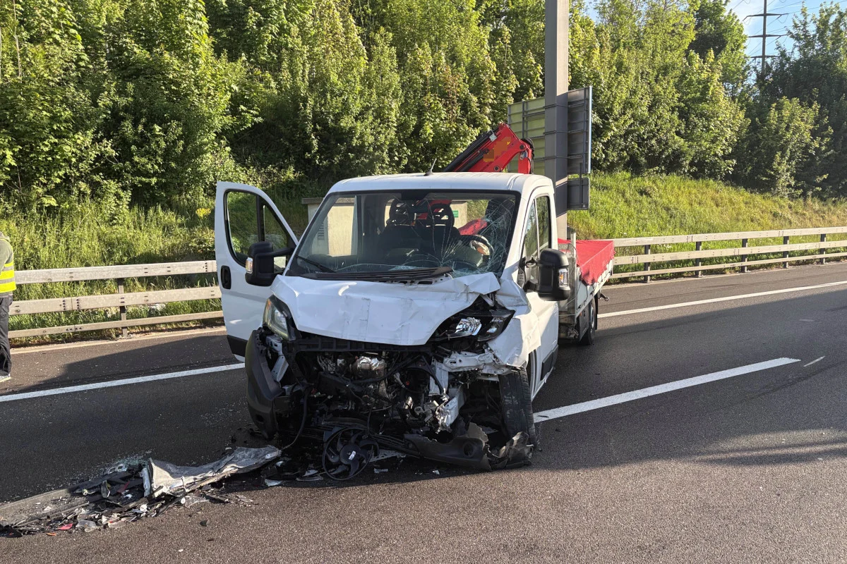 Ein beschädigter Transporter steht auf einer Fahrspur der Autobahn, die Front ist stark eingedrückt. Links im Bild eine teilweise sichtbare Person in Sicherheitsweste.