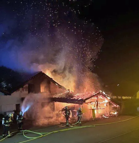 Ein brennendes Haus wird in der Nacht von Feuerwehrleuten gelöscht. Flammen und Rauch steigen auf.