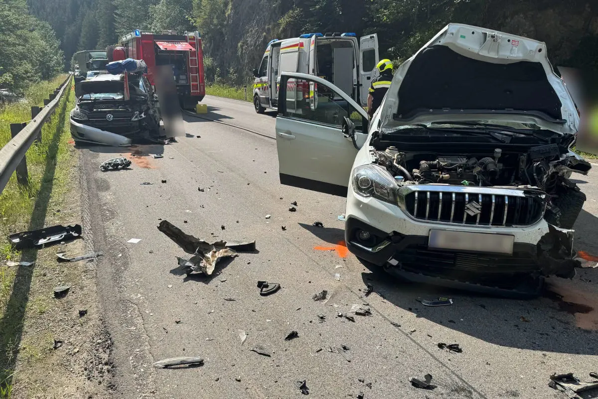 Zwei stark beschädigte Autos stehen auf einer Straße, Trümmerteile sind verteilt. Ein Feuerwehrfahrzeug im Hintergrund.