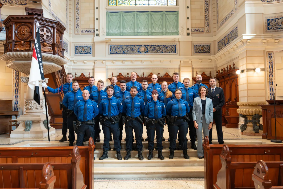 Eine Gruppe von Polizisten in blauen Uniformen steht in einem kunstvoll dekorierten, historischen Raum auf einer Treppe. Sie posieren vor einer Holzkanzel und tragen den Schriftzug 'Polizei' auf ihren Uniformen.