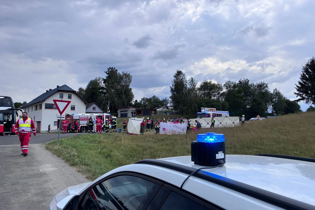 Mehrere Einsatzkräfte und Rettungsfahrzeuge sichern eine Unfallstelle auf einer Landstraße bei bewölktem Wetter. Ein Polizeifahrzeug mit Blaulicht ist im Vordergrund zu sehen.