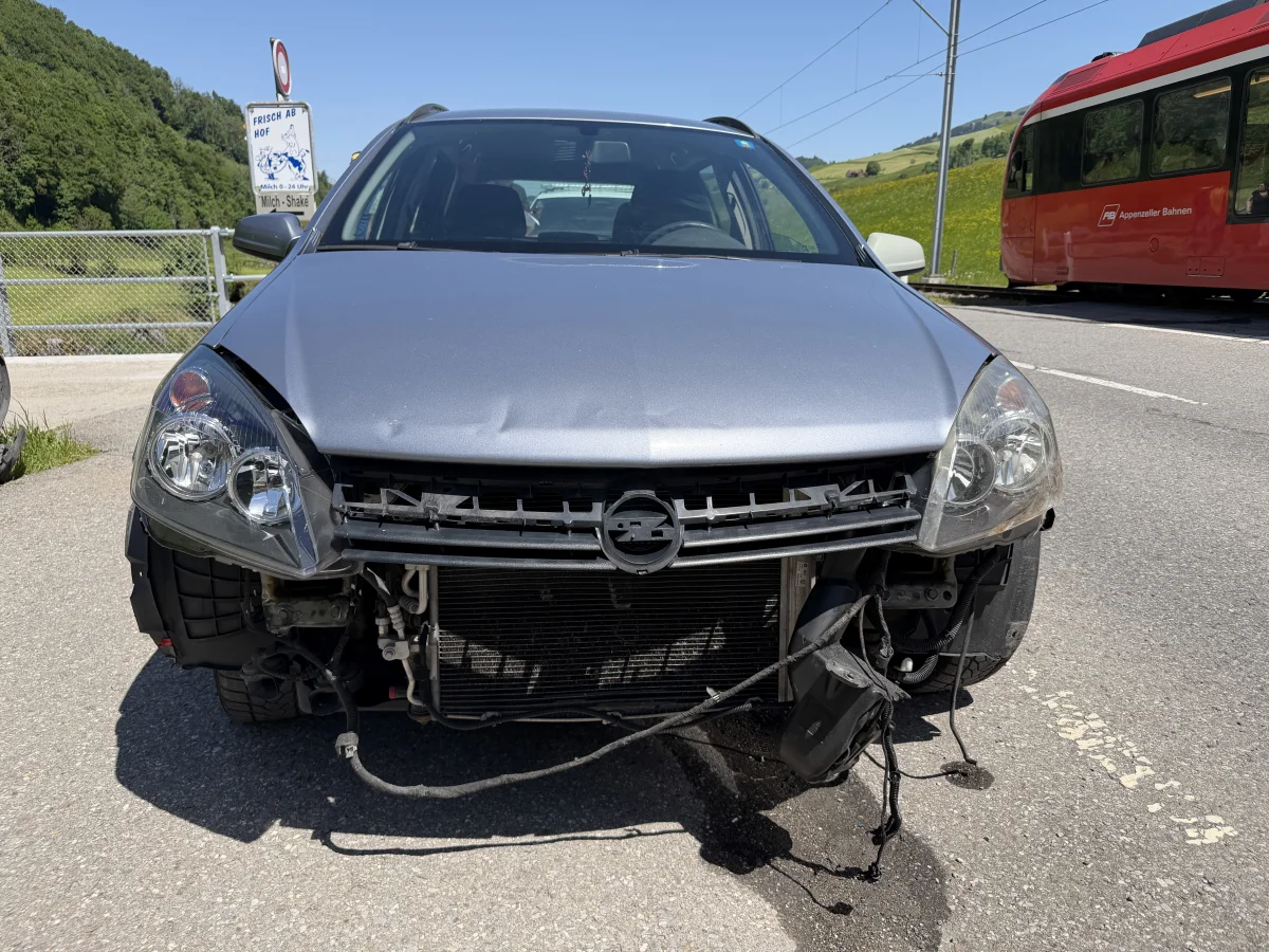 Ein silberner Opel ist erheblich an der Front beschädigt. Im Hintergrund ist ein roter Zug der Appenzeller Bahnen zu sehen.