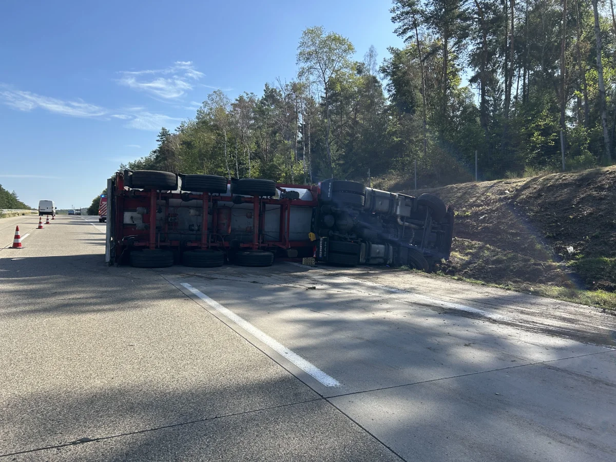 Ein großer Lkw liegt auf der Seite, blockiert die rechte Spur einer Autobahn. Der Himmel ist klar und sonnig.