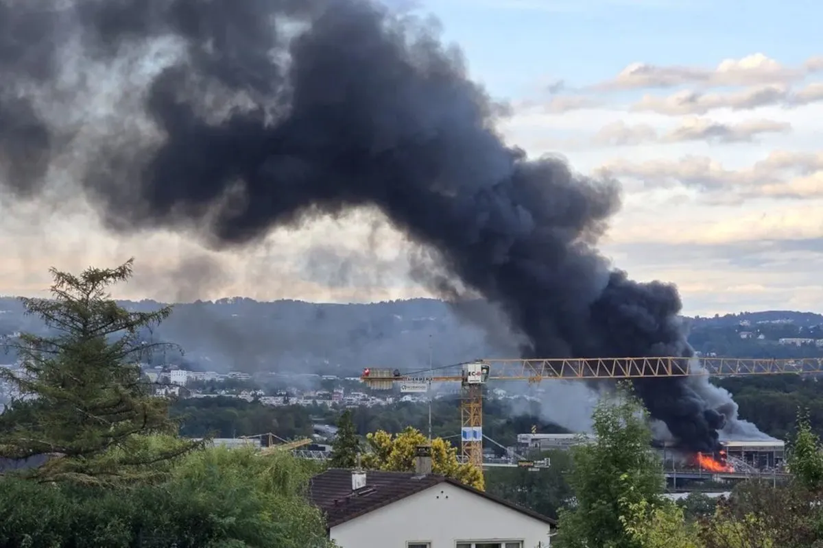 Dichter schwarzer Rauch steigt von einem großen Gebäudebrand im Hintergrund auf. Ein Kran steht nahe dem Brandherd.