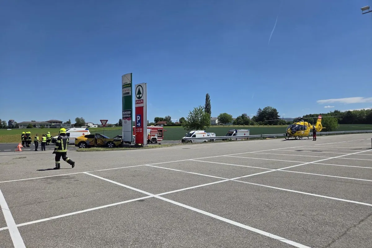 Einsatzkräfte umgeben ein verunfalltes Auto an einer Tankstelle im Freien. Ein Rettungshubschrauber steht in der Nähe.