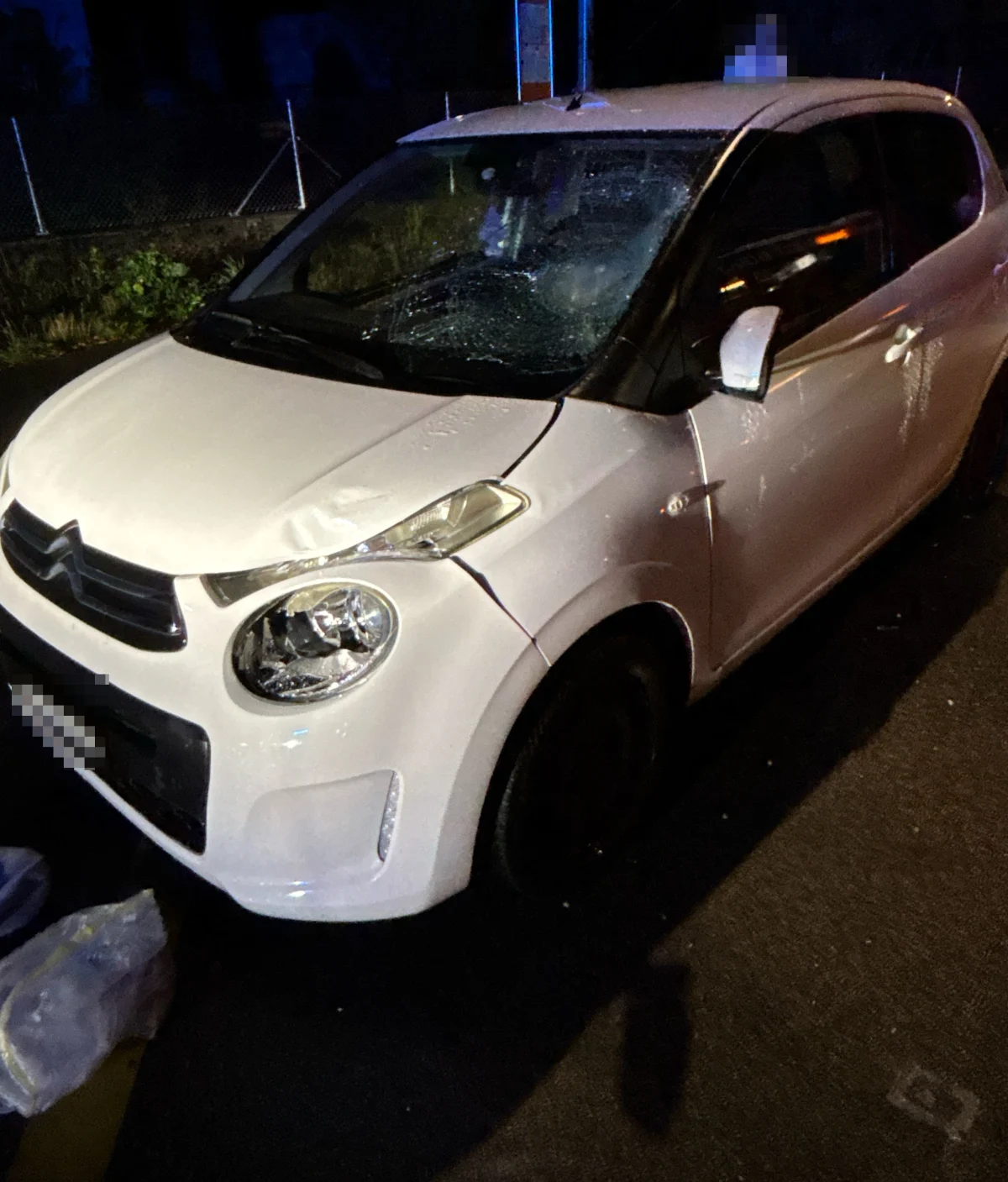 Ein weißer Citroën steht am Straßenrand, die Windschutzscheibe ist stark beschädigt. Um das Fahrzeug herum sind keine Personen sichtbar.