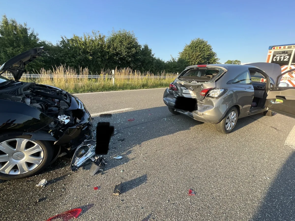 Zwei Autos stehen mit sichtbaren Schäden auf einer Landstraße. Ein Fahrzeug hat einen deformierten Vorderbereich, das andere Schäden am Heck.