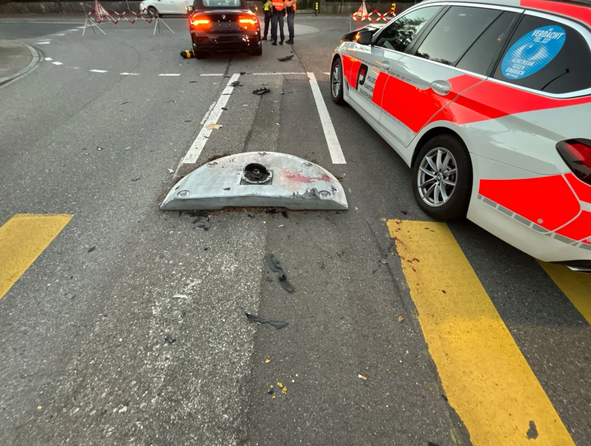 Ein beschädigter Kanaldeckel liegt auf der Straße, umgeben von Trümmerteilen. Ein Polizeiauto ist neben der Unfallstelle sichtbar.