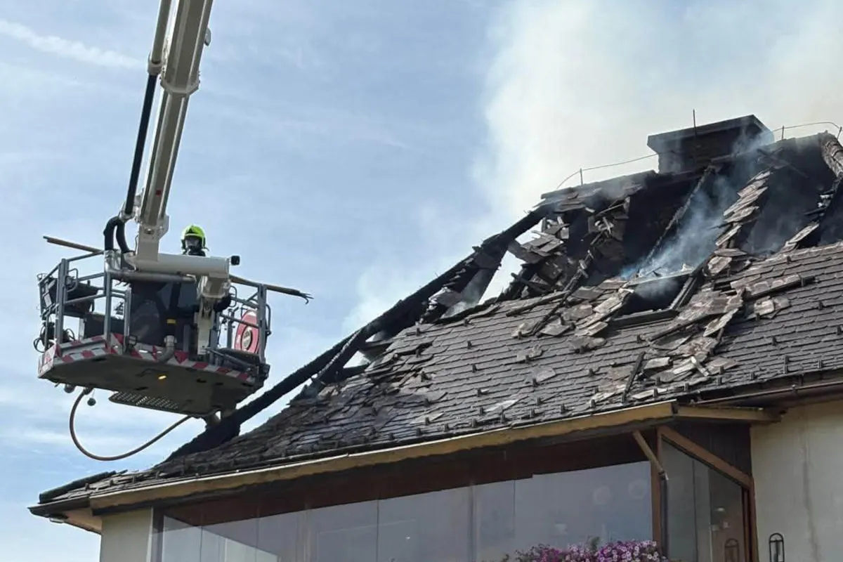 Ein Feuerwehrmann in Schutzausrüstung löscht von einem Hubsteiger aus ein stark beschädigtes und rauchendes Dach.