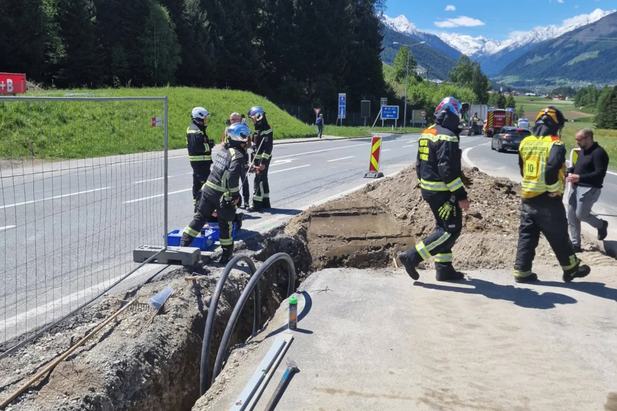 Mehrere Einsatzkräfte stehen bei einer abgesperrten Baustelle auf einer Landstraße. Im Hintergrund sind Bäume und Berge zu sehen.