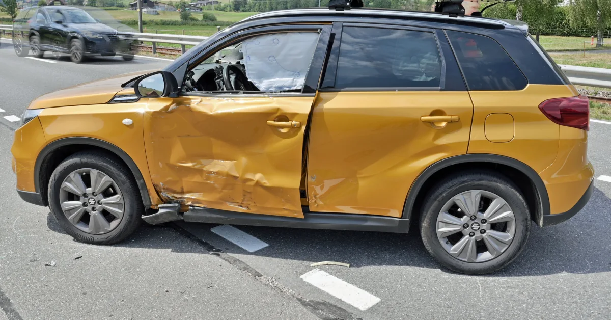 Ein goldener SUV steht mit einem schweren Seitenschaden auf der Straße. Im Hintergrund ist ein weiteres Fahrzeug zu sehen, das die Szene passiert.