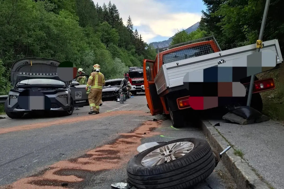 Ein Verkehrsunfall zeigt mehrere beschädigte Fahrzeuge auf einer Landstraße, umgeben von Bäumen, mit Feuerwehrleuten vor Ort.