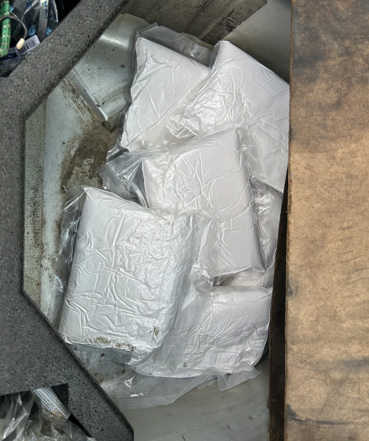 In einer versteckten Kammer eines Fahrzeugs befinden sich mehrere weiße, in Plastik verpackte Päckchen. Diese scheinen sorgfältig verborgen worden zu sein.