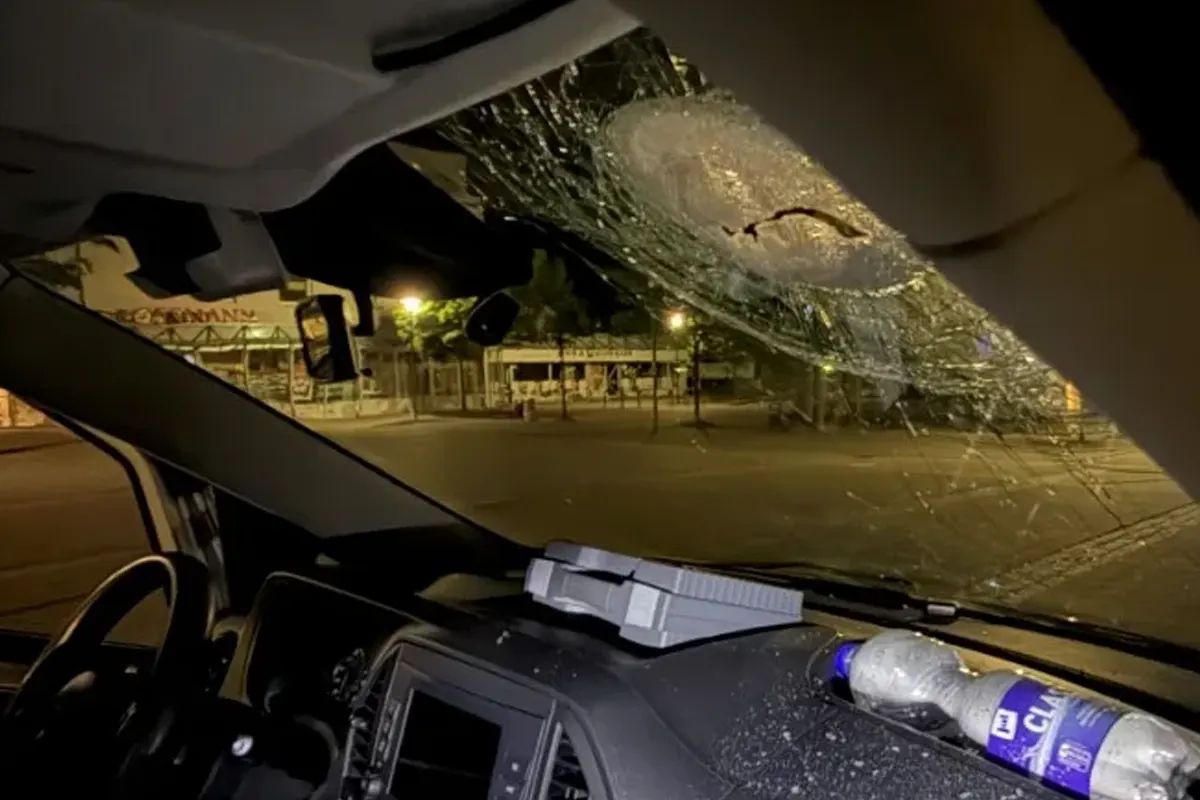 Das Bild zeigt die Innenseite einer Windschutzscheibe mit einem großen Riss und gesplittertem Glas. Im Vordergrund sind das Lenkrad und das Armaturenbrett eines Fahrzeugs erkennbar.