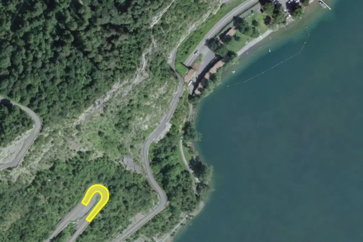 Eine Haarnadelkurve auf einer Straße verläuft durch bewaldetes Gelände und führt entlang eines großen Sees.