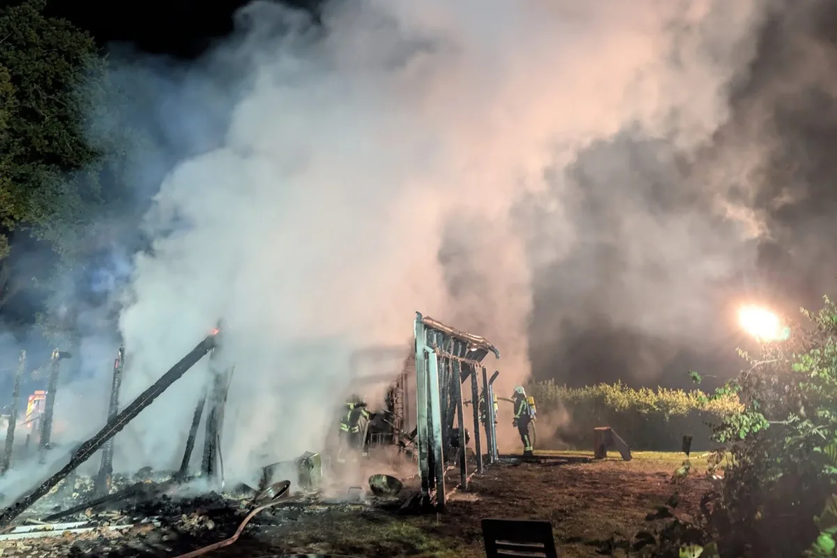 Bei Nacht versuchen zwei Feuerwehrleute, einen stark qualmenden Gebäudebrand zu löschen. Dichte Rauchschwaden sind sichtbar.