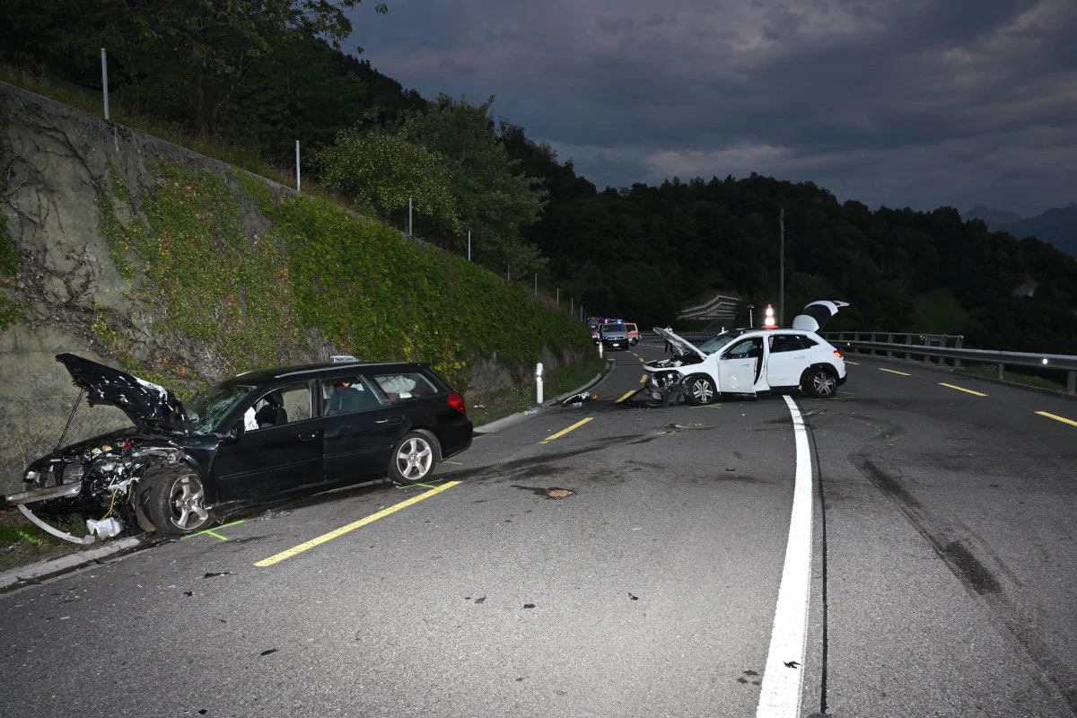 Zwei stark beschädigte Fahrzeuge stehen nach einer Kollision auf einer kurvigen Landstraße. Im Hintergrund sind Bäume und Berge zu sehen.