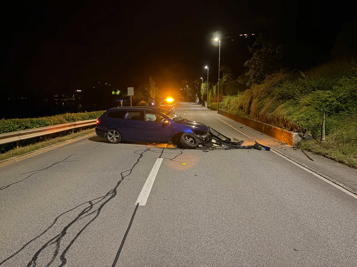 Ein beschädigtes blaues Auto steht quer auf einer beleuchteten Straße, offensichtlich nach einem Unfall mit einer Leitplanke.