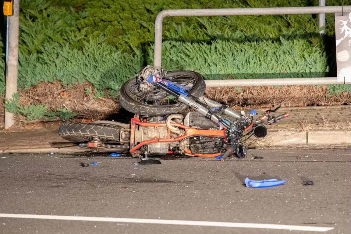 Ein beschädigtes Motorrad liegt auf der Seite der rechten Straßenseite. Um das Fahrzeug sind Glassplitter und Trümmer zu sehen.