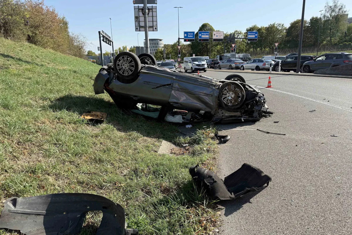 Ein Auto liegt auf dem Dach neben einer Autobahnrampe, umgeben von Trümmern und Verkehrsschildern.