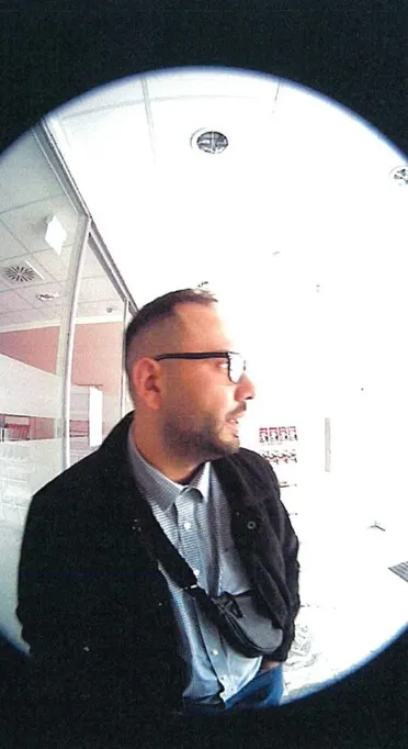Ein Mann mit Brille und Bart steht in einem Büro und schaut zur Seite. Die Aufnahme ist körnig mit Fisheye-Effekt.