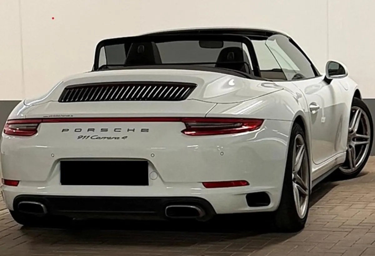 Ein weißer Porsche 911 Carrera 4 steht in einem Parkhaus. Das Fahrzeug ist von hinten sichtbar und hat ein geschlossenes Verdeck.