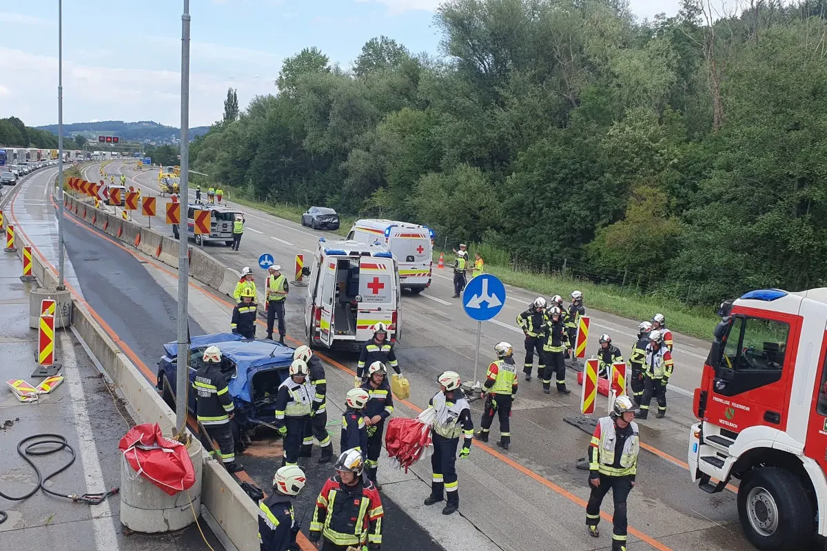 Ein auf der Seite liegendes Auto auf einer Autobahn, umgeben von Feuerwehrleuten und Rettungsfahrzeugen. Rettungsdienste stehen bereit.
