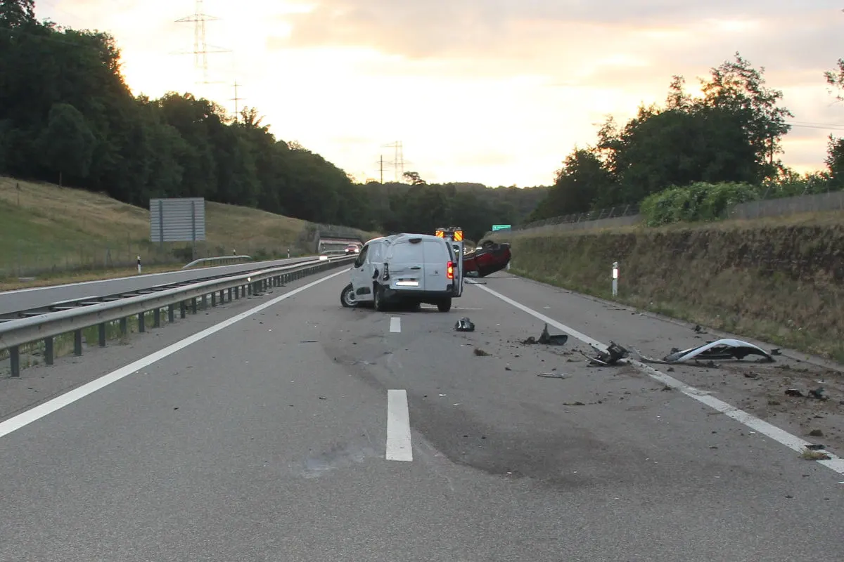 Ein weißer Transporter liegt seitlich auf der Autobahn, umgeben von Trümmerteilen und Absperrungen. Ein weiteres Fahrzeug ist im Hintergrund sichtbar.