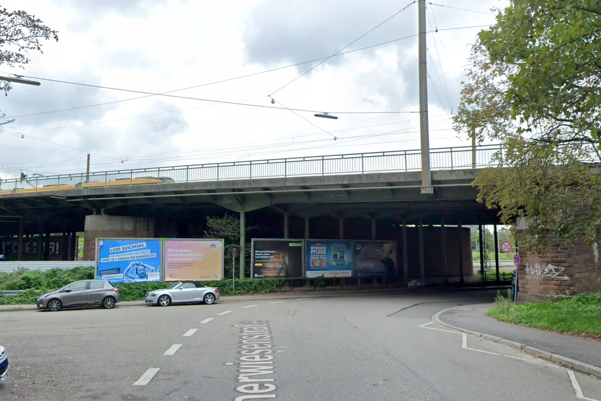 Zwei Autos sind unter einer Eisenbahnbrücke geparkt. Die Umgebung ist eine städtische Straße, es ist bewölkt.
