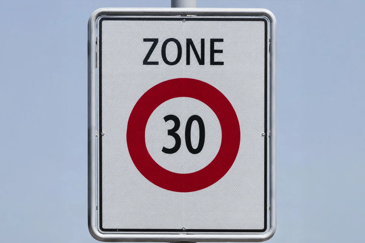 Ein Verkehrsschild zeigt eine Geschwindigkeitsbegrenzung von 30 km/h an. Es befindet sich vor einem klaren blauen Himmel.