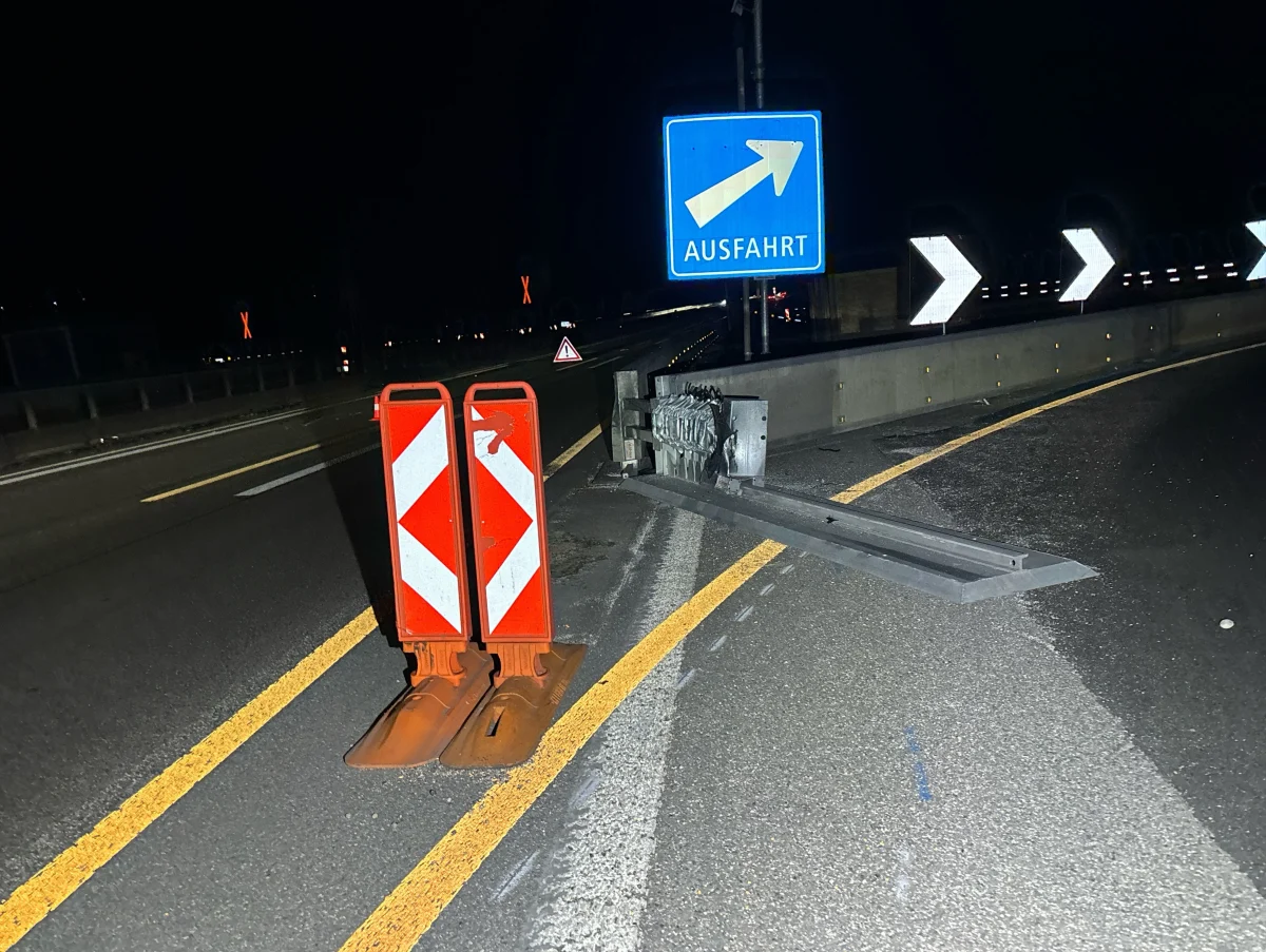 Bei Nacht zeigt das Bild eine beschädigte Leitplanke neben einem blauen 'Ausfahrt'-Schild. Warnschilder sind ebenfalls sichtbar.