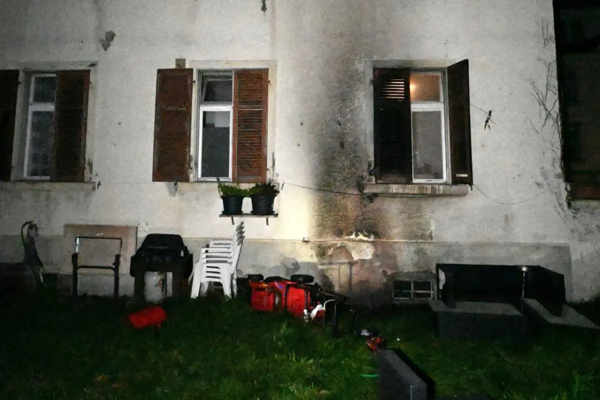 Die Fassade eines Wohnhauses zeigt Brandspuren. Im Vordergrund sind Gartenmöbel und andere Objekte zu sehen.
