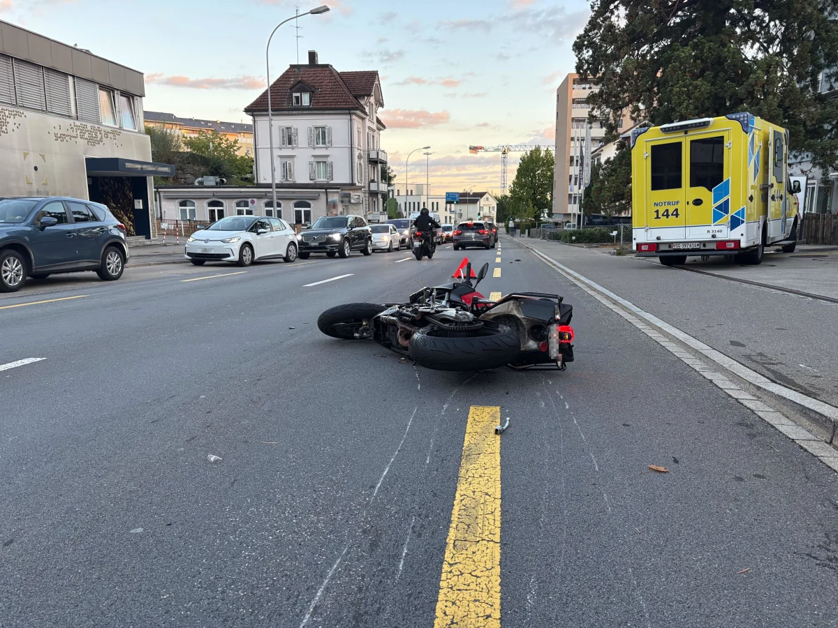 Auf der Straße liegt ein umgestürztes Motorrad. Im Hintergrund ist ein gelber Krankenwagen sowie mehrere parkende Autos zu sehen.