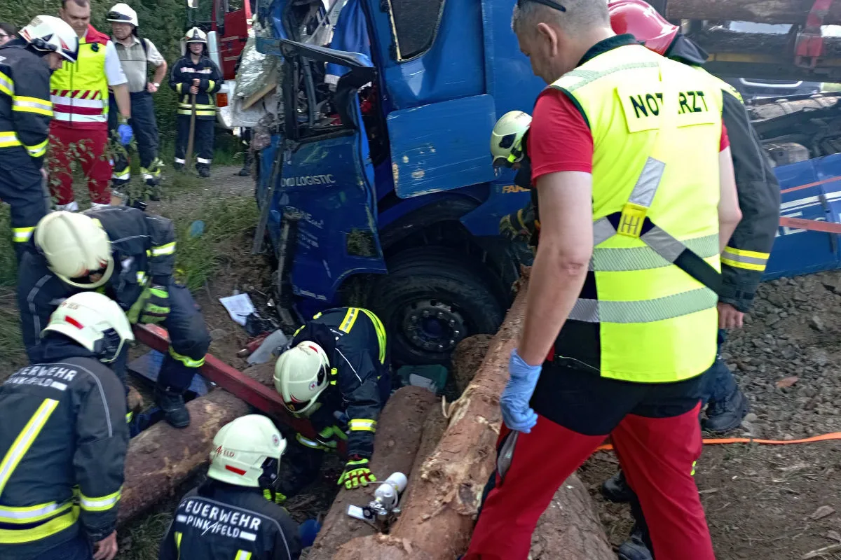 Mehrere Rettungskräfte arbeiten daran, jemanden aus einem blauen Lastwagen zu retten, der mit Holz beladen ist. Der Notarzt ist ebenfalls vor Ort.