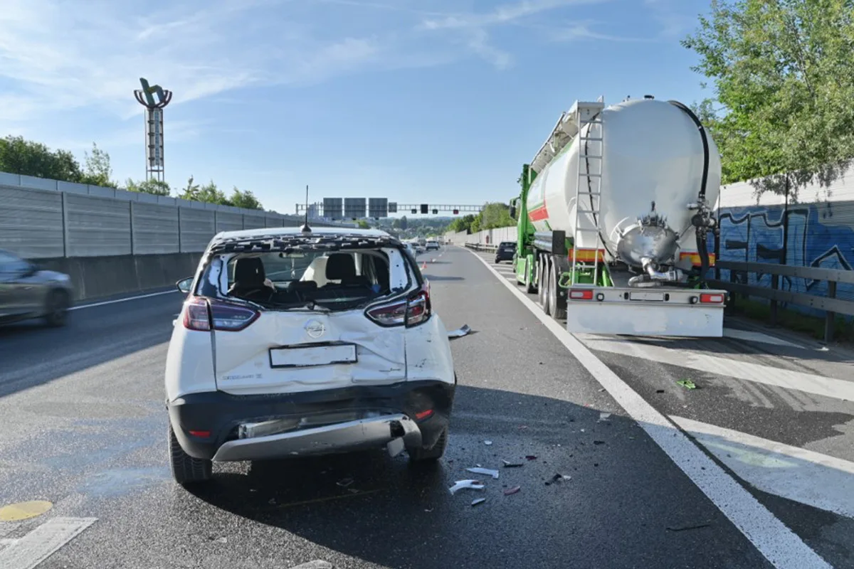 Ein weißes Auto mit deutlichen Heckschäden steht auf einer Autobahn mit einem Tanklastwagen daneben. Trümmerteile sind auf der Straße verstreut.