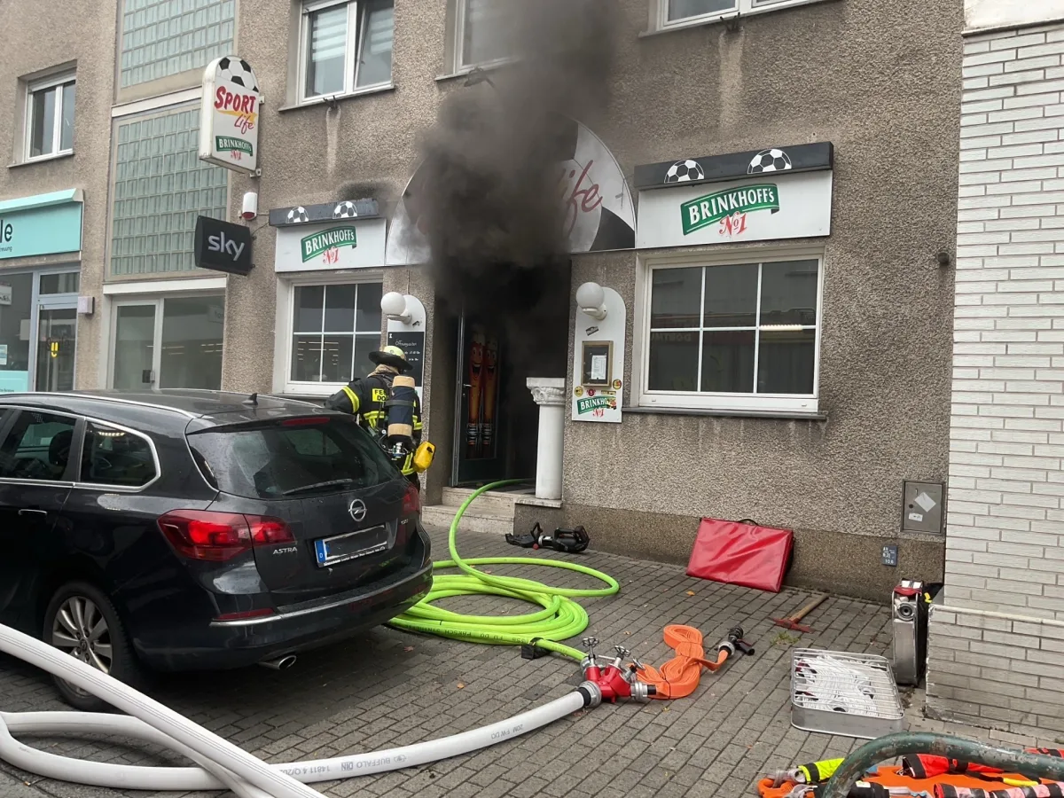 Ein Feuerwehrmann steht vor einem verrauchten Eingang eines Gebäudes. Feuerwehrschläuche liegen auf dem Boden.