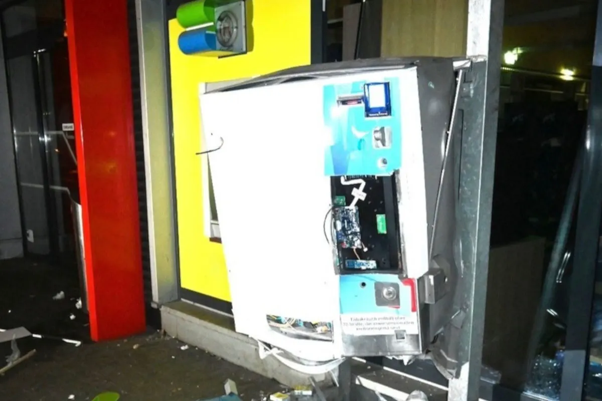 Ein Geldautomat steht in einem Vorraum und ist stark beschädigt, mit sichtbarer innerer Technik und Elektronikteilen.