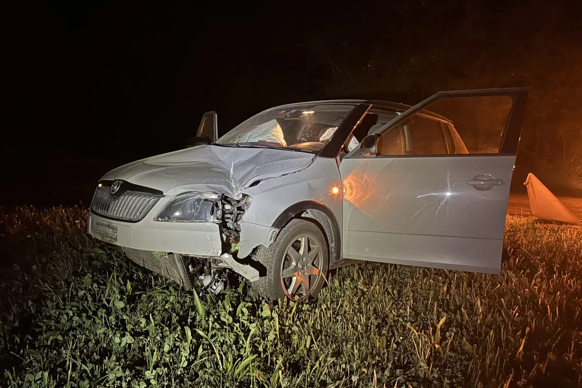 Ein weißes Auto mit stark beschädigtem Frontbereich steht auf einer Wiese. Die Fahrertür ist geöffnet, und es ist Nacht.