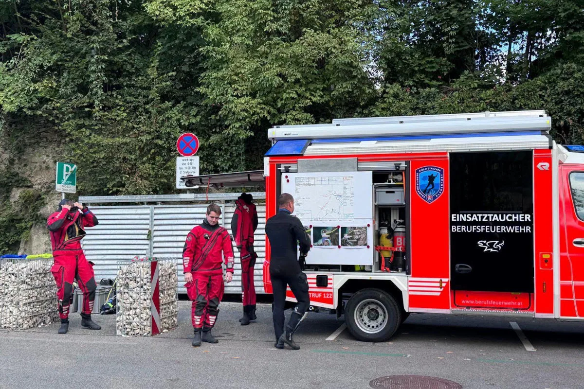 Ein Feuerwehrfahrzeug ist zu sehen, daneben stehen mehrere Personen in roten Taucheranzügen. Eine Tafel mit Kartenmaterial ist am Fahrzeug montiert.