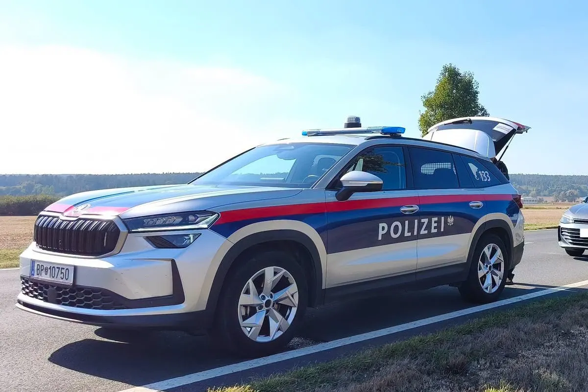 Ein österreichisches Polizeiauto steht am Straßenrand mit geöffnetem Kofferraum. Es ist ein klarer Tag, leichte Vegetation im Hintergrund.