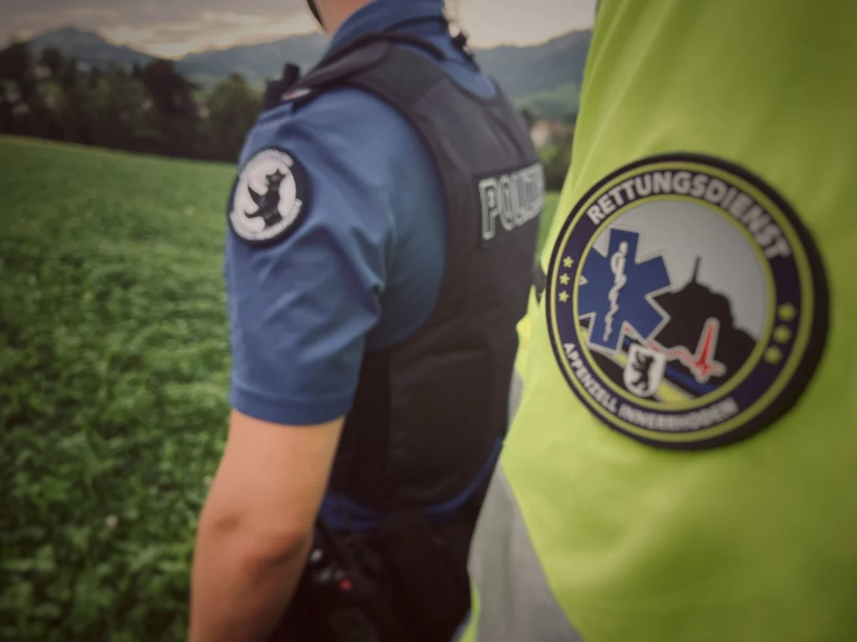 Zwei Personen, eine von der Polizei in blauem Hemd, die andere vom Rettungsdienst in gelber Jacke, stehen auf einem Feld.
