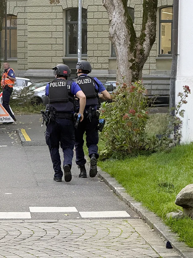 Zwei Polizisten in taktischer Ausrüstung gehen auf einem Bürgersteig. Ein weiterer Polizist steht im Hintergrund.