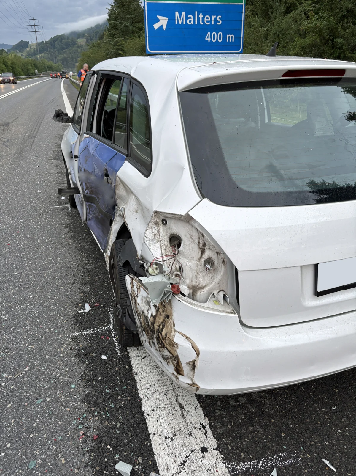 Ein weißes Auto mit sichtbarem seitlichen Schaden steht auf dem Pannenstreifen. Im Hintergrund ist ein Ausfahrtschild nach Malters zu sehen.